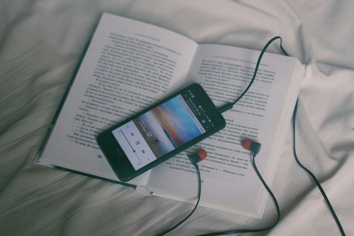 Smartphone playing music plugged into earphones on a book.