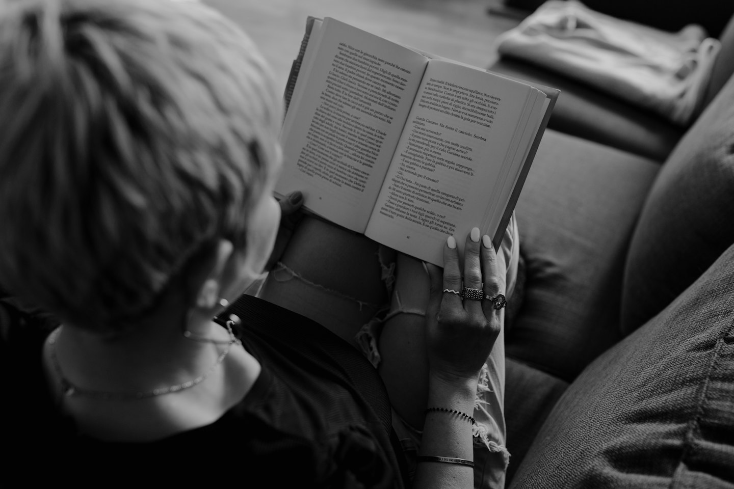 Person with rings reading a paperback book on a sofa.