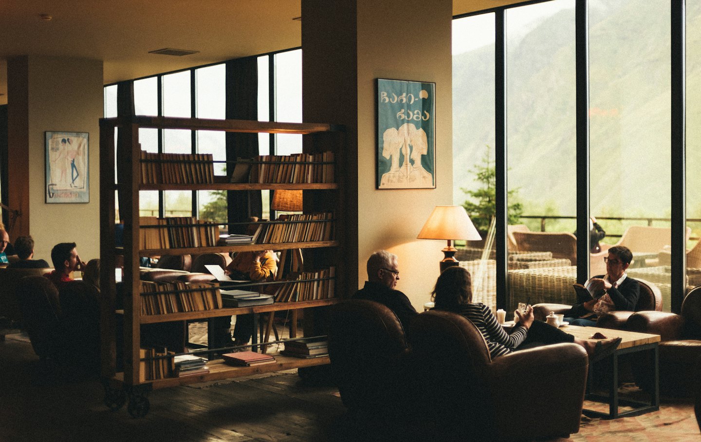 People relax in a lounge with bookshelves and mountain views.